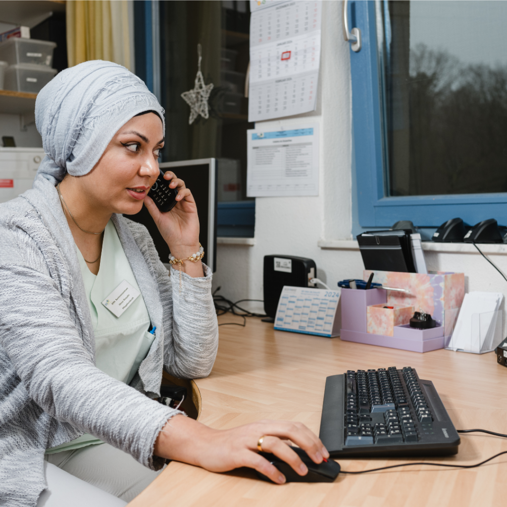 Eine Pflegekraft im BSH Seniorenzentrum arbeitet am Schreibtisch, telefoniert und navigiert gleichzeitig am Computer